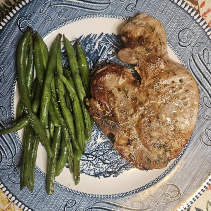 a rosemary pork chop and green beans on a blue plate