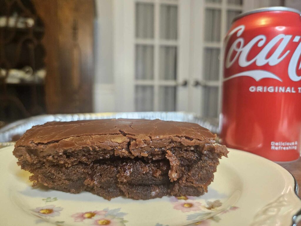 a slice of Coca Cola cake sits on a plate in front of a can of coke